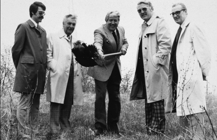 A man with shovel surrounded by other men for groundbreaking.